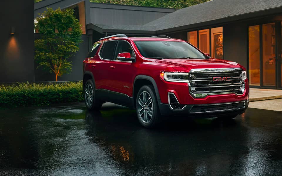 A red Acadia parked on the street, in front of a building.